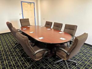 Travelodge by Wyndham Fort Wayne North في فورت واين: قاعة اجتماعات مع طاولة وكراسي خشبية