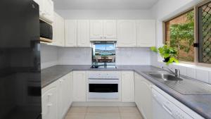 Una cocina con gabinetes blancos y un fregadero y una ventana. en Roweshaven Amazing Views, Close To Beach Accom Holidays, en Terrigal