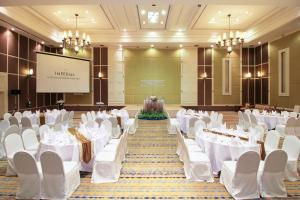 un salón de banquetes con mesas y sillas blancas y una pantalla en The Imperial Hotel & Convention Centre Korat, en Nakhon Ratchasima