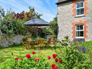 a table and chairs with an umbrella in a garden at Poplar Farm Cottage in Westbury-sub-Mendip