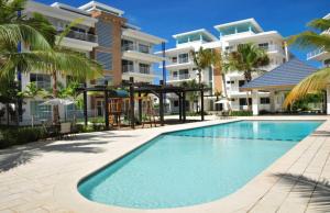 a swimming pool in front of a building with palm trees at Lumina at Jardines Punta Cana Village in Punta Cana