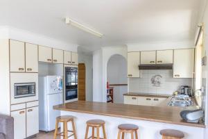 a kitchen with white cabinets and bar stools at Peaceful Cul de sac in Sussex inlet