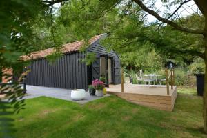 een zwarte schuur met een houten terras in een tuin bij Red Poll Barn in Spexhall