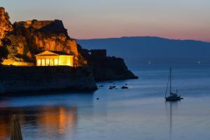 a boat in the water with a building on a cliff at Sun Corfu near the airport in Corfu Town