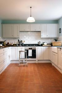 una cocina con armarios blancos y taburete. en Gardener's House - Hawarden Estate en Hawarden