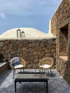 2 chaises et une table en face d'un mur en pierre dans l'établissement Kirani Resort, à Pantelleria