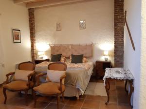 een slaapkamer met een bed met 2 stoelen en een tafel bij BnB Ferme Beauregard Les Pyrénées in Artigat