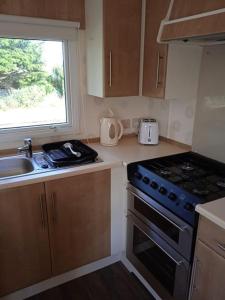 cocina con fogones, fregadero y ventana en Seaside Holiday Home St. Osyth, Essex 2 Bathroom, 6 Berth with Country Views en Saint Osyth