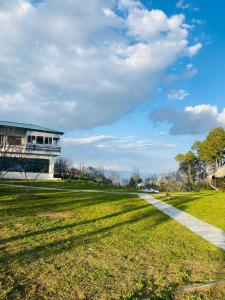 a grassy field with a building and a sidewalk at Nitya Village Retreat in Chamba