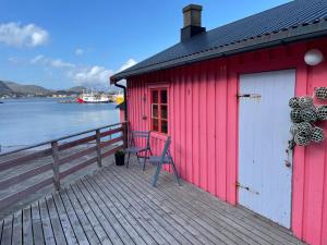 a red building with a chair on a dock at Kræmmervika Rorbuer - Rustic Cabins in Lofoten in Ballstad