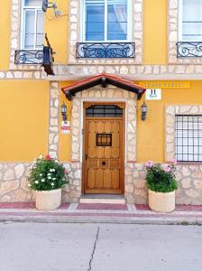 un edificio giallo con una porta in legno e due piante di Hostal Cañamares a Cañamares