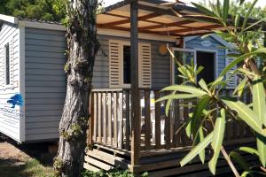 a blue tiny house with a porch and a tree at Mobilhome «La mouette rieuse» * 6 personnes *Climatisatisé *2 Chambres in Sigean