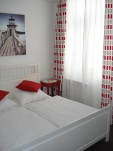 1 dormitorio con cama blanca y almohada roja en Kleines Logierhaus 05, en Norderney