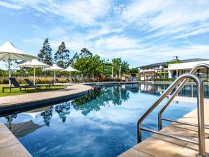 a swimming pool with chairs and umbrellas at Mercure Kooindah Waters Central Coast in Wyong