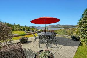 a table and chairs with a red umbrella on a patio at Skyfall Glencoe at Creag an-t Sionnaich in Glencoe