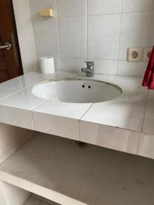 a white sink in a white tiled bathroom at Rumahku Bali Executive in Kuta