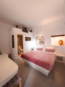 a white bedroom with a large bed with red sheets at Aggelikoula Rooms in Tinos