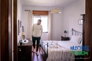 a man standing in a bedroom with a bed at Casa do Mirante in Praia da Vitória