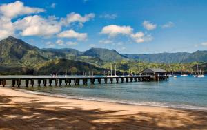 a pier on a beach with mountains in the background at Kaiana Villa in Princeville