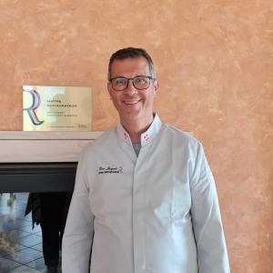 um homem de óculos em frente a uma mesa em LA SOURCE Jacquet depuis 1954 Hôtel et Studio em Saint-Jean-de-Chevelu