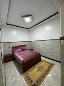 Schlafzimmer mit einem Bett mit lila Bettwäsche und einem Teppich in der Unterkunft Bel Appartement 1er Étage confortable près de la plage - spécialement pour familles in Saidia 