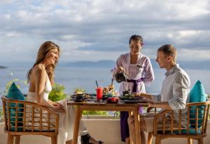 grupa trzech osób siedzących przy stole z jedzeniem w obiekcie Pramana Natura Nusa Penida w mieście Nusa Penida