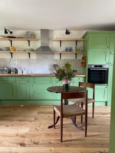 eine Küche mit grünen Schränken und einem Tisch mit Blumen darauf in der Unterkunft Peaceful cottage with private garden in Hailsham