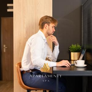 un hombre sentado en una mesa usando un ordenador portátil en Apartamenty SPA z prywatnym Jacuzzi & Sauną, en Białystok