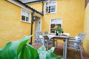 a patio with a table and chairs and a yellow wall at Aldeburgh Cottage in Aldeburgh