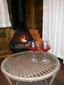 two glasses of wine sitting on a table with a fireplace at Cabana Sítio Costãozinho in Bom Retiro