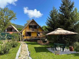 Casa amarilla con mesa y sombrilla en Cosy Mountain Villa in Nizepole en Bitola