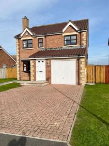 una casa de ladrillo con un garaje blanco en una entrada de ladrillo en Rockview Beadnell - Perfect Family Retreat, en Beadnell