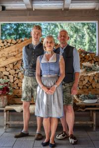 a woman and two men standing in front of a cabin at Hotel Landhaus Tirolerherz in Sankt Ulrich am Pillersee