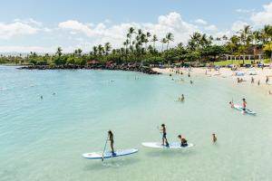 um grupo de pessoas em pranchas de surf na água em uma praia em The Islands at Mauna Lani Point - CoralTree Residence Collection em Waikoloa