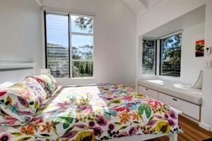 a bedroom with a bed with a colorful comforter and two windows at Eureka in Boomerang Beach