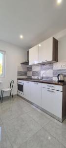 a kitchen with white cabinets and a table and a chair at Apartments Ana i Ante Punta in Milna