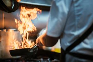 a person cooking food in a pan on a stove at Mercure Launceston in Launceston