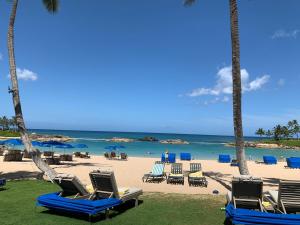 a beach with chairs and palm trees and the ocean at Ko Olina Ocean View Home Office in Kapolei
