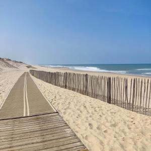 a wooden boardwalk on a beach next to the ocean at Studio maubuisson lac/océan 4/6 personnes in Carcans