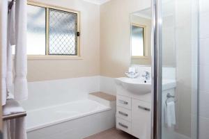a white bathroom with a bath tub and a sink at Reflections Lennox Head - Holiday Park in Lennox Head