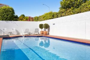 una piscina con sillas y una pared blanca en Villa Aqua Riverside Retreat with Pool, en Noosaville
