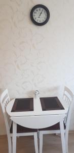 une table blanche avec deux chaises et une horloge sur le mur dans l'établissement Apart Sauliaus, à Klaipėda
