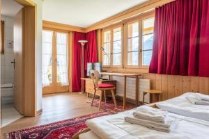 a hotel room with two beds and a desk and red curtains at Apartment Schneerose - GRIWA RENT AG in Grindelwald