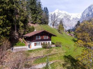 une petite maison sur une colline avec des montagnes en arrière-plan dans l'établissement Chalet Lienzhubel - GRIWA RENT AG, à Grindelwald