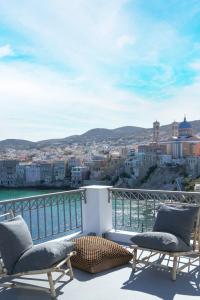 a balcony with two chairs and a view of a city at Pafsilipon Suites in Ermoupoli