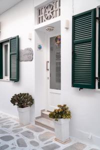 una casa blanca con persianas verdes y dos macetas en Aggelikoula Rooms, en Tinos