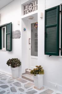 a white house with green shutters and two potted plants at Aggelikoula Rooms in Tinos