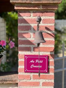 a bell hanging on a brick wall with a sign at Chambre d hôte petit crussac in Mauvezin