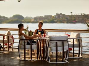 Sonesta St George Nile Cruise - Luxor to Aswan 4 Nights from Monday to Friday في الأقصر: رجل وامرأة يجلسون على طاولة بجانب الماء