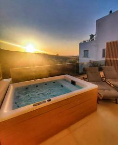 bañera de hidromasaje en un balcón con vistas a la puesta de sol en el fondo en L A Boutique Suites with Private Hot Tub, en Kalathas